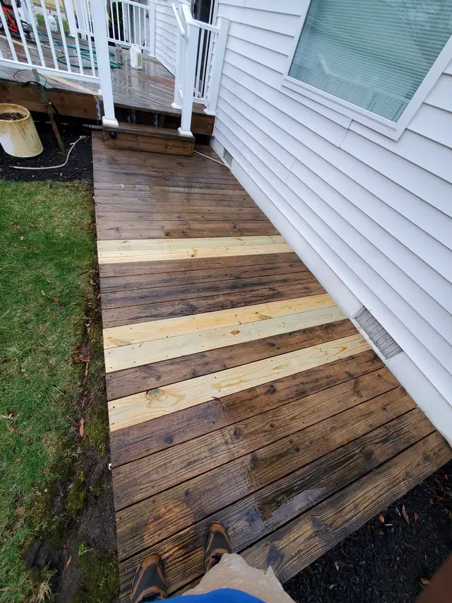 Deck walkway with new pale pine boards let in among washed, older boards