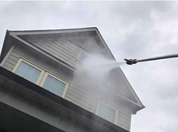 Low-pressure wash fanning across a grey-sided gable under white trim