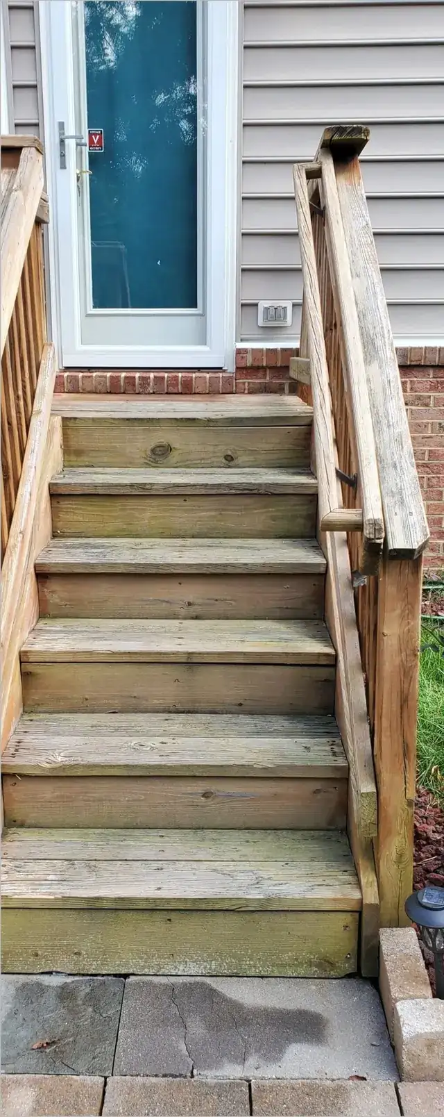 Grey, weathered deck stairs and handrail with green staining on the treads